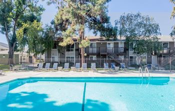 A swimming pool in front of a building with trees and chairs around it.